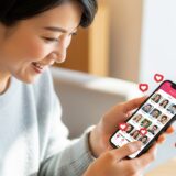 スマートフォンを見ながら微笑む20代〜30代の日本人女性。明るいカフェや自宅のリビングなどリラックスした雰囲気